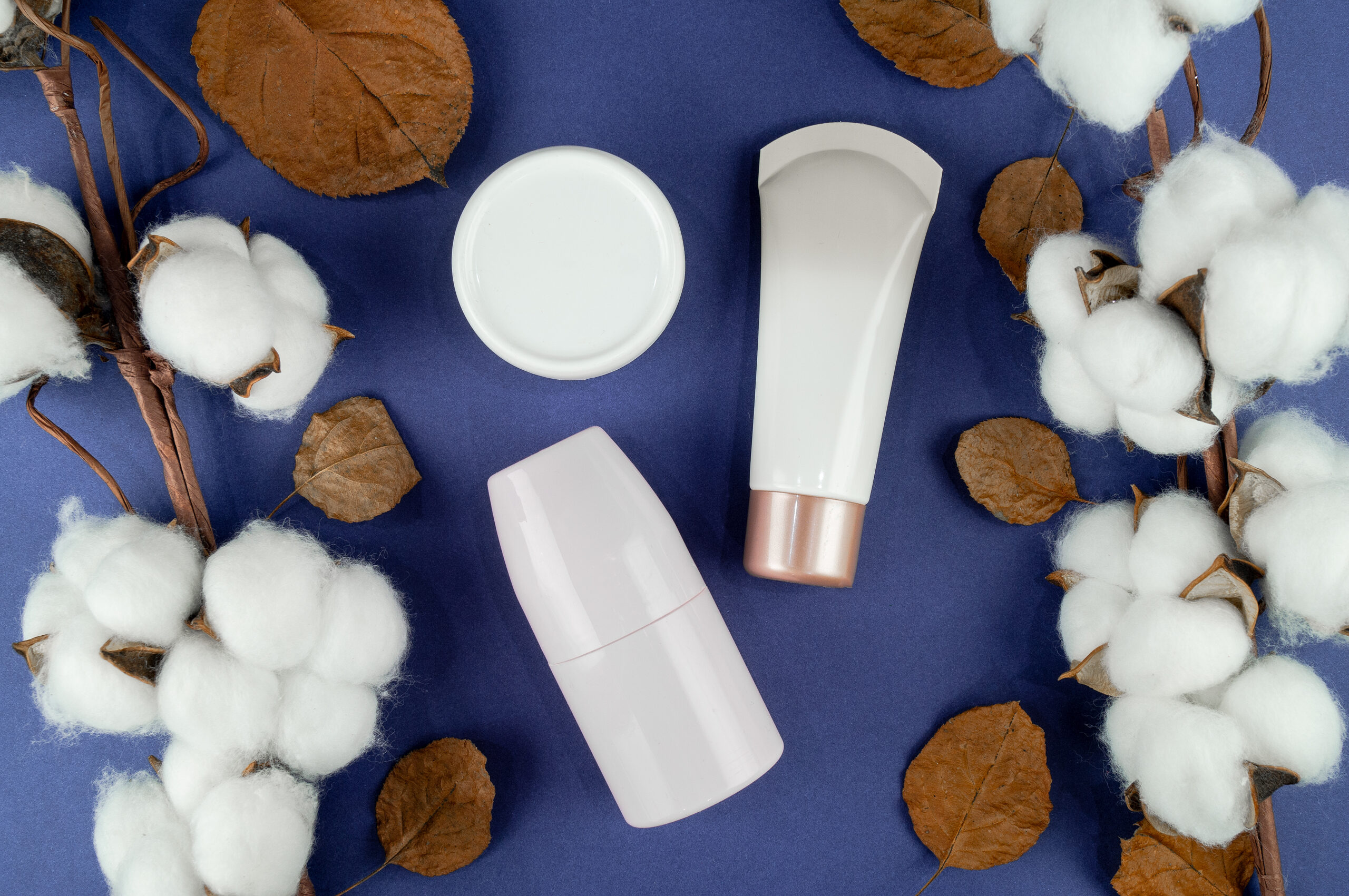 Cream jars on a background of cotton and leaves. An indicator of the natural product. Mockup on a blue background